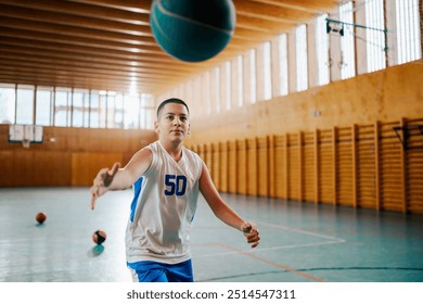 A young basketball player focuses on passing the ball during a game in an indoor court, capturing the essence of kids in sport - Powered by Shutterstock