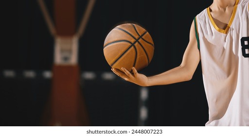 Young basketball player holds classic ball. Basket in background. Junior level basketball player holding game ball. Basketball training session for kids - Powered by Shutterstock