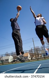 A Young Basketball Player Shooting The Basketball And His Opponent Trying To Block It.