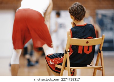 Young Basketball Player Watching Basketball Practice Drill. Boy Sitting on Wooden Chair and Resting During School Basketball Training. Basketball Camp For Kids - Powered by Shutterstock