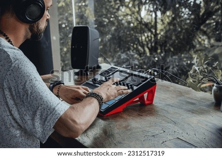 Young beard man make music at synthesizer and laptop, listen music on headphones, music artist