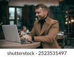 Young beard man using laptop on office, freelance work, outdoor close up hipster portrait, brutal, guy listening music on earphones, make photo and video, production, Bali, coffee cup, smartphone