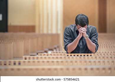 Young beard man wearing blue shirt praying in modern church