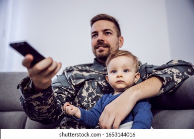 Young bearded brave soldier spending quality time with his beloved son. They are watching television. Man having remote control in hands. - Shutterstock ID 1653144016