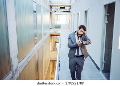 Young Bearded Businessman Looking At Wristwatch And Talking With Business Partners. He Is Late For Meeting And Making Excuse. Building In Construction Process Interior.