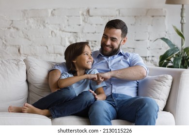 Young bearded father his little adorable smiling son sit together on couch in living room, fist bumping, making hand gesture, showing unity, express respect, feeling attachment, family ties concept