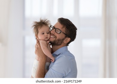 Young Bearded Father Holding Sweet Baby, Hugging Adorable Infant, Touching Cheek-to-cheek, Cuddling With Love, Express Care, Feeling Affection Standing Indoors. Happy Fatherhood, Family Bond Concept