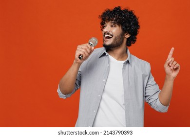 Young bearded Indian man 20s years old wears blue shirt sing song in microphone dance sing song fooling around have fun gesticulating hands enjoy isolated on plain orange background studio portrait