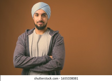 Young bearded Indian Sikh man wearing turban against brown background