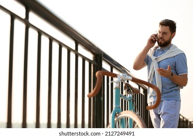 Young Bearded Man With Bicycle Talking By Mobile Phone On Embankment