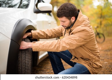 Young Bearded Man Checking Car Tyre In Autumn Forest