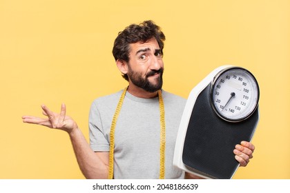 young bearded man dieting doubting or uncertain expression and holding a sweight scale