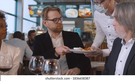 Young bearded man dining with friends returning poor cooked dish to waiter in mask. Irritated businessman refusing unappetizing meal in cafe during lunch with colleagues - Powered by Shutterstock