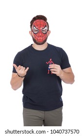 A Young Bearded Man Doing The Spider Man Movement With His Hand And Holding A Little Toy For Spiderman Character And Putting His Mask, Isolated On A White Background.