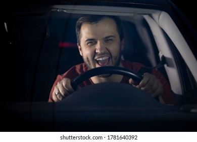 A Young Bearded Man Drives A Car, Holds The Steering Wheel With Both Hands And Laughs. Driving On Highways At Night. Street Racing. The Joy Of Overtaking A Car In A Race.