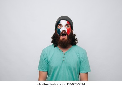 Young Bearded Man With Face Painted In French Flag Colors Staring At The Camera.