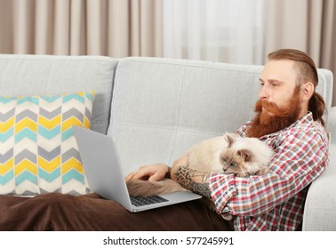 Young Bearded Man With Fluffy Cat Using Laptop At Home