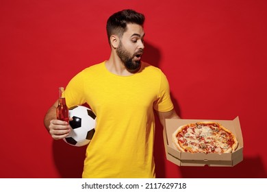 Young bearded man football fan in yellow t-shirt cheer up support favorite team hold soccer ball look at italian pizza in cardboard flatbox beer isolated on plain dark red background studio portrait - Shutterstock ID 2117629718