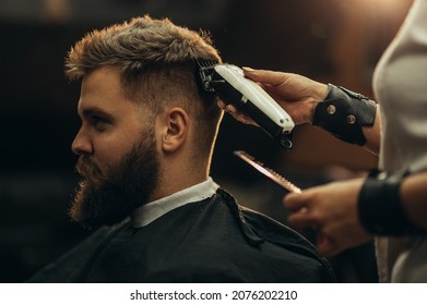 Young bearded man getting haircut by hairdresser while sitting in chair at barbershop - Powered by Shutterstock