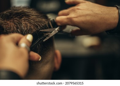 Young bearded man getting haircut by hairdresser while sitting in chair at barbershop - Powered by Shutterstock