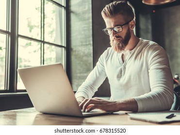 Young bearded man in glasses using a laptop while working in the office