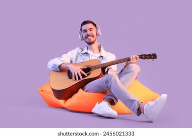 Young bearded man in headphones playing guitar on lilac background - Powered by Shutterstock