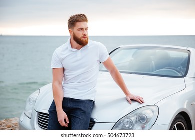 Young bearded man leaning on his car parked on beach - Powered by Shutterstock