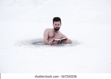 young bearded man reading a book in the water ice of the lake