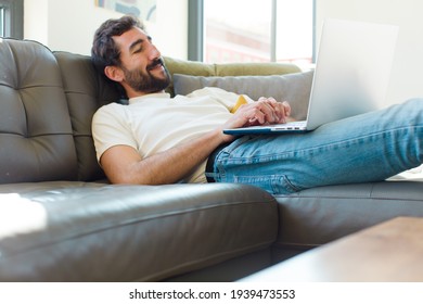 Young Bearded Man Resting On A Couch With A Laptop