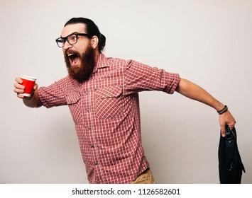 Young Bearded Man Running Wearing Glasses, Is Late To Work, Coffee To Go. Young Man Scared To Be Late, In A Hurry Or Rush. Rush Hour Concept.