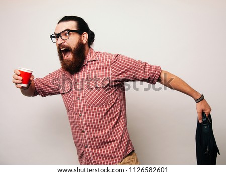 Young bearded man running wearing glasses, is late to work, coffee to go. Young man scared to be late, in a hurry or rush. Rush hour concept.