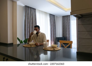 Young Bearded Man Sitting While Eating Breakfast Alone At Home