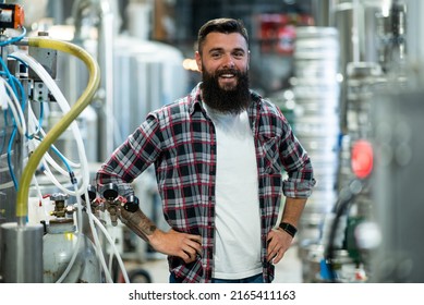 Young bearded man standing by beer filling machine and posing. Brewery worker with industrial equipment. Looking into the camera. Wearing checkered shirt and smiling. - Powered by Shutterstock