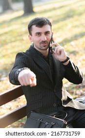 A Young Bearded Man Is Talking On The Phone And Pointing His Finger At The Camera. A Businessman Gesturing While Talking On The Phone
