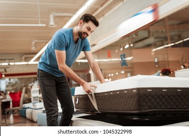 Young bearded man is testing mattress in furniture store. Orthopedic mattress for a healthy posture. Checking mattress in furniture store.
