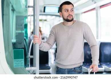 Young bearded man traveler riding in modern streetcar, standing leaning on suitcase and holding on to handrails .. - Powered by Shutterstock