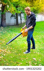 A Young Bearded Man Using A Cordless, Electric Leaf Blower In A Garden. Garden Works. Autumn, Fall Gardening Works In A Backyard, On A Lawn, Grass.