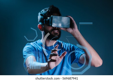 Young Bearded Man In VR-headset Over Dark Blue Background Is Touching A Virtual Interactive Screen