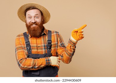 Young bearded man wear straw hat overalls work in garden point finger aside indicate on workspace mock up isolated on plain pastel light beige color background studio portrait. Plant caring concept - Powered by Shutterstock