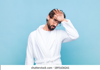 young bearded man wearing a bath robe looking stressed, tired and frustrated, drying sweat off forehead, feeling hopeless and exhausted