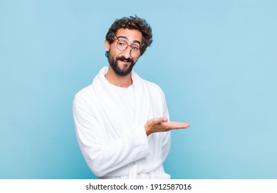 Young Bearded Man Wearing A Bath Robe Smiling Cheerfully, Feeling Happy And Showing A Concept In Copy Space With Palm Of Hand