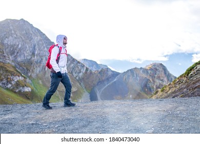 Young Bearded Man Wearing White Puff Jacket Standing Near A Mountain