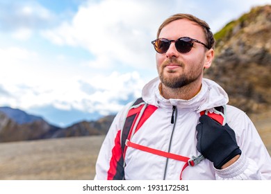 Young Bearded Man Wearing White Puff Jacket Standing Near A Mountain