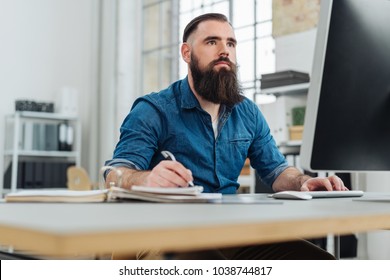 Young bearded man working at desk in front of monitor during office work - Shutterstock ID 1038744817