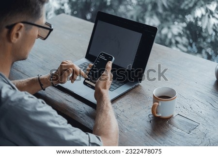 Young bearded man works on a laptop, uses a smartphone, a freelancer, a computer, financial analyst, a sales manager, prepares a report, charts, crypto-currencies in cafe, hipster, beard brutal. 