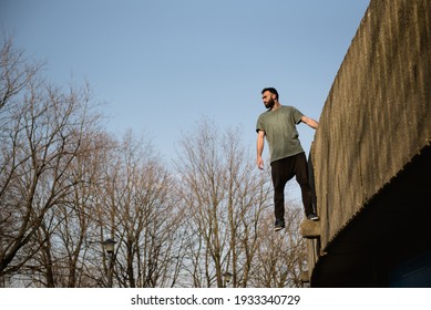 A Young Bearded Parkour Man Standing On A High Wall. 