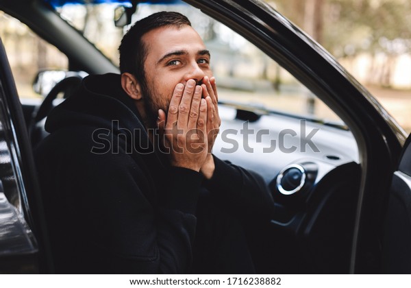 Young\
bearded scared man stare at camera, touch cheeks, closed mouth,\
being frightened of difficulties, express great shock, wear casual\
shirts. Man sitting in the car and look\
surprised.