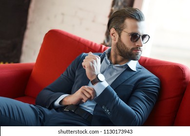 Young bearded stylish businessman leader indoors at office wearing sunglasses with watch looking aside serious