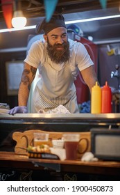 Young Beardy Hipster Working In Fast Food Service, Wearing Cook Hat 