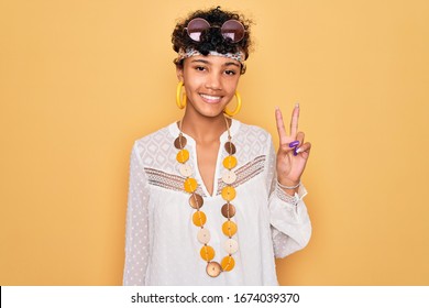 Young beautiful african american afro hippie woman wearing sunglasses and accessories showing and pointing up with fingers number two while smiling confident and happy.